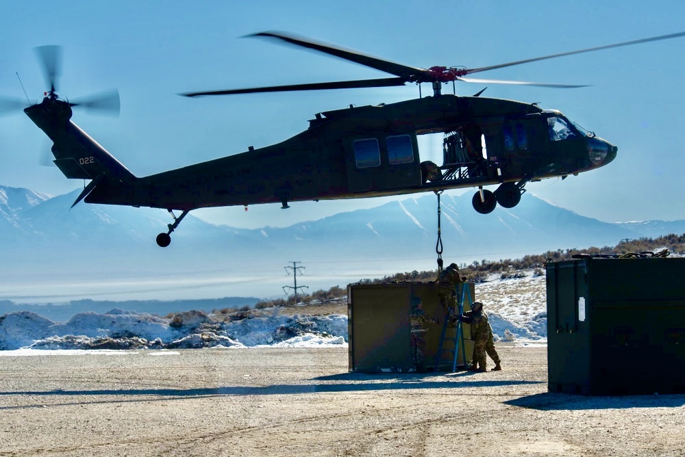 Crew rigging a kitchen container beneath a hovering Black Hawk